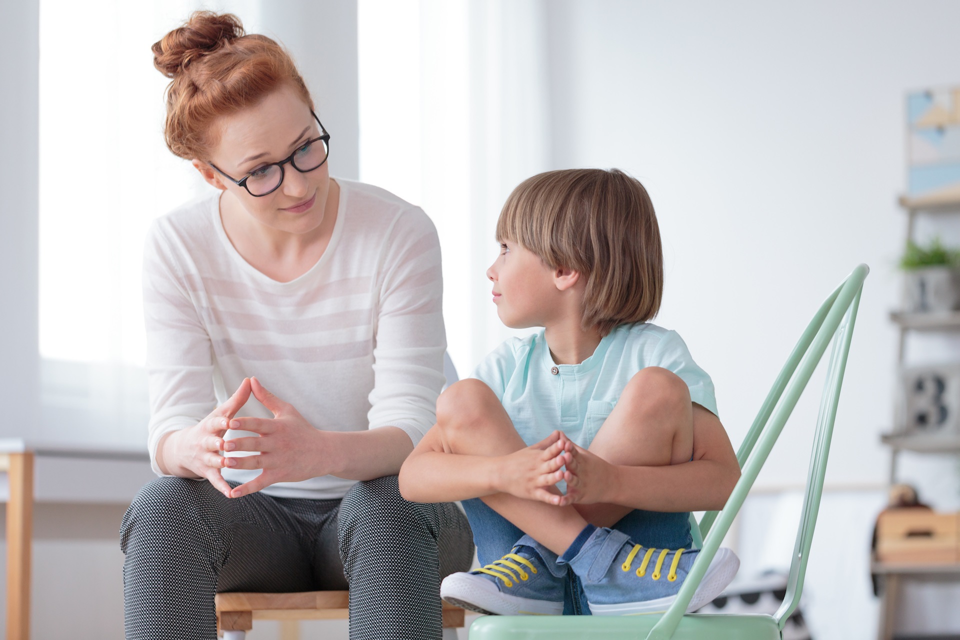 Young female school psychologist having serious conversation with smart little boy at office